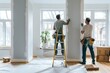© blinkstud.io - Two male workers from the professional home renovation service painting walls light gray in a living room interior inside a new modern house or apartment