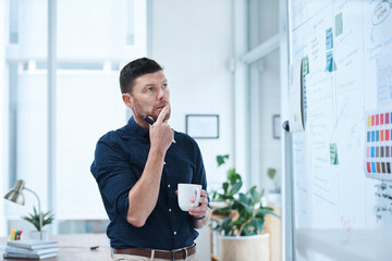 Poster - Man, thinking and coffee in office for brainstorming with whiteboard, thoughts and planning for day ahead or designer tasks. Project manager, ideas and strategy for campaign schedule and goal setting