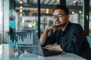 Wall Mural - A businessman sits at a desk in a modern office, thoughtfully reviewing data displayed on his laptop screen