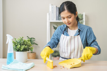 Wall Mural - Household clean up, housekeeper asian young woman wearing protection rubber yellow gloves, using broom, dustpan sweeping remove spilled crumb food broken on dirty table at home, equipment for cleaning