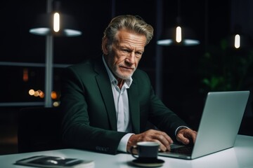 confident senior businessman using laptop while sitting at illuminated desk in creative office