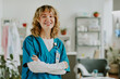 © AnnaStills - Golden haired Caucasian nurse smiling widely and crossing her arms while sitting for portrait in on call room