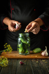 Wall Mural - A man adds garlic to a jar of cucumbers before pickling them on the kitchen table. Concept of pickling delicious cucumbers with spices at home