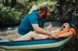 © qunica.com - A joyful couple laughing and playing in a hammock by a serene river, surrounded by nature. Captures fun, love, and outdoor relaxation.