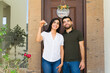 © AntonioDiaz - Newlywed couple happily posing in front of their new home with keys and a welcome sign