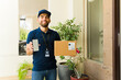 © AntonioDiaz - Smiling delivery man holding a package and showing a smartphone with a blank screen at a house entrance