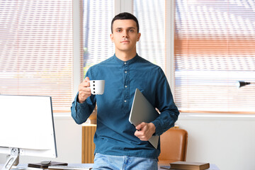 Sticker - Handsome young man with laptop and cup of coffee in office