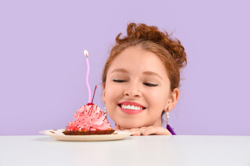 Wall Mural - Beautiful young happy woman with birthday cupcake on table against purple background