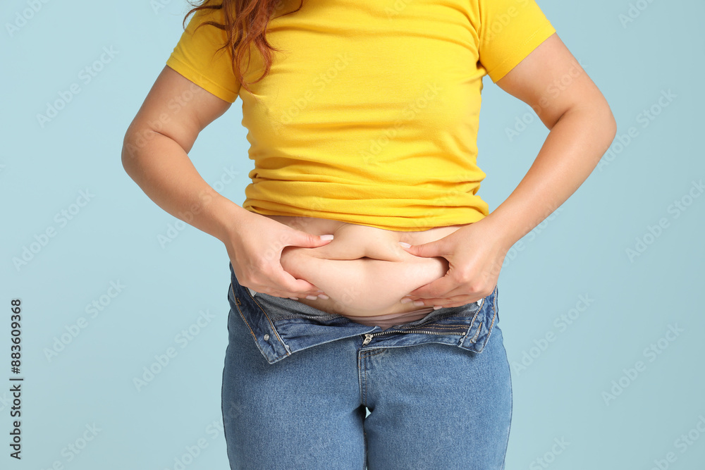 Overweight woman in tight jeans on blue background. Excess weight concept