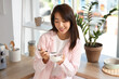 © Pixel-Shot - Pretty young Asian woman in pajamas eating tasty yogurt at home