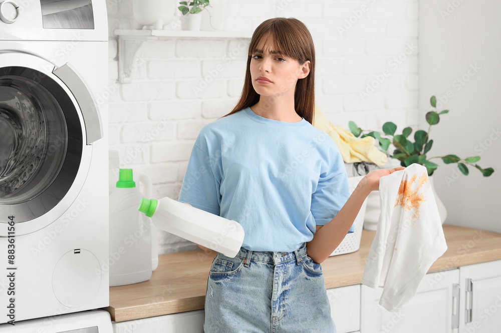 Young woman with stained clothes and detergent in laundry room