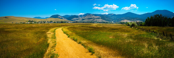 Wall Mural - Tranquil rural dirt road curving through the prairie toward Lolo National Forest in Helena, Montana