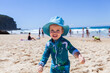 © Austockphoto - Happy toddler wearing hat for sun protection at beach playing in sand
