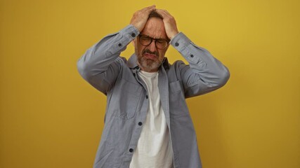 Wall Mural - Hispanic man, middle age, wearing glasses, standing, suffering from a headache, pain, and stress, holding head with hands, migraine ache, over isolated yellow background