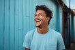 © Gmbr_bmny - Close-up portrait of a cheerful man wearing an blue shirt and glasses, laughing joyfully against a dark background.