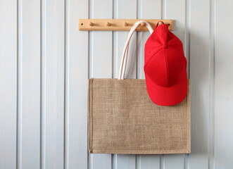 summer bag and a red baseball cap hang on a wooden hanger on a white board wall in the cottage. Concept: plastic-free, natural interior. copy space.