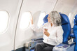 © NanSan - An adult woman sits by the window on a passenger plane, eagerly traveling abroad. She gazes at the clouds, anticipating new experiences and adventures in a foreign land.