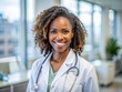 © Sirinporn - Confident African American female doctor beams with warmth and professionalism in a sterile clinic office, making eye contact with a gentle, reassuring smile.