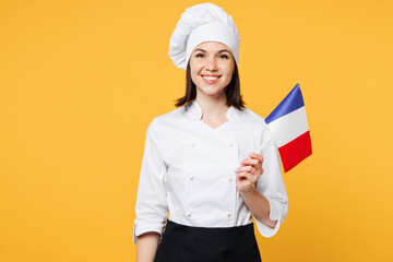 Wall Mural - Young smiling happy chef cook baker woman wears white shirt black apron uniform toque chefs hat hold in hand French flag looking camera isolated on plain yellow background studio Cooking food concept