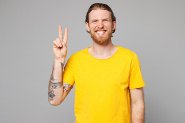 Wall Mural - Young smiling happy fun joyful positive Caucasian man he wears yellow t-shirt casual clothes showing victory sign looking camera isolated on plain grey background studio portrait. Lifestyle concept.