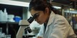 © ds17 - Female scientist focused on using a microscope in a laboratory, conducting important research.