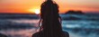 © Jevjenijs - A woman facing the ocean, her back to the viewer, at sunset