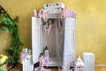 Wall Mural - Flowering pink wisteria tree blooming. White vintage wardrobe and suitcases on it decorated blooming wisteria flowers. Elegant wedding decor photo zone. Cascades of Purple Wisteria close-up. 