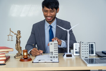 Asian businessman in a formal suit works alone at a lawyer's desk with golden scales, a law book, leather bags, and a Lady Justice statue, reflecting personal freedom and legal responsibilities.