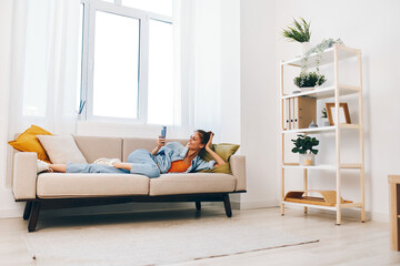 Relaxing at Home: Young Woman Smiling and Holding Mobile Phone on Cozy Sofa in Living Room