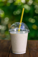 Poster - vanilla flavor milkshake or protein cocktail in disposable plastic glass with straw on table outdoors