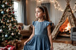 © Alex Vog - Portrait of child cover girl in blue dress posing at Christmas tree and wigwam, thinking looking away. Face of pensive kid girl 7 year old in children room. Christmas magic concept. Copy ad text space
