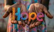 © Nadin Faust - photo of the text hope in colorful letters held by two african children's hands, outstretched hand, blurred background, vibrant colors, childlike innocence