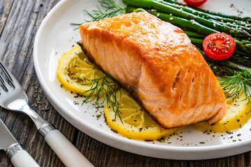 Sticker - Fried salmon steak with cooked green asparagus, cherry tomatoes and lemon slices served on white plate on  wooden table