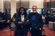 © Flamingo Images - Two smiling young businesswomen standing together in the lobby of an office building