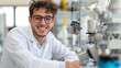 © Elena - A smiling young scientist in a lab coat is standing next to advanced laboratory equipment. Enthusiastic and promising young researcher in a cutting-edge laboratory environment.