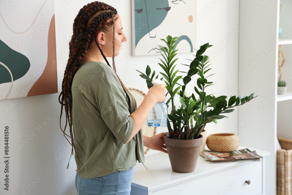 Young woman with dreadlocks watering plant at home