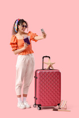 Poster - Young African-American woman taking selfie with passport and ticket near suitcase on pink background