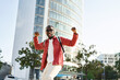 © insta_photos - Authentic photo of happy excited young African Black man student hipster winner wearing headphones, sunglasses and backpack feeling joy having fun listening music and dancing on city street outdoors.