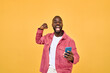 © insta_photos - Happy Black man winner holding smartphone celebrating win isolated on yellow. Excited African young gen z guy holding cellphone. Amazed user sport betting game app winner using mobile phone.