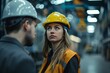 © Jane_S - Engineer in hard hat conversing with colleague in a factory, indicating a project review.