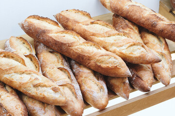 Poster - A row of bread loaves are on a wooden shelf. The loaves are all different sizes and shapes, but they all have a similar appearance. The bread looks fresh and inviting