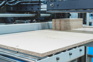 Poster - A stack of wooden boards Chipboard are being cut by a machine. The boards are all the same size and are lined up on a conveyor belt