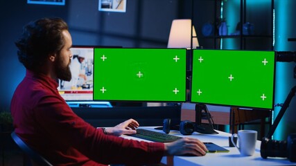 Wall Mural - Photographer using photo editing software on Chroma key multi monitors setup to improve images quality. Photo editor utilizing pictures retouching application on green screen display