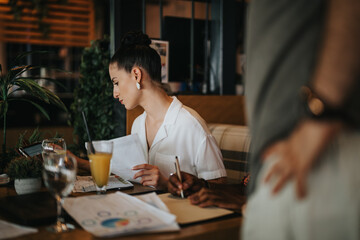 Wall Mural - Businesspeople collaborating during a meeting in a coffee bar, reviewing documents and engaging in productive discussion.