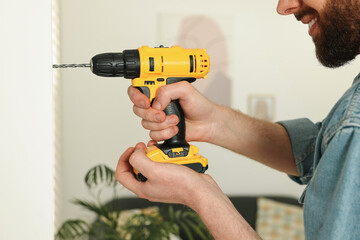 Sticker - Smiling man drilling white wall at home, closeup