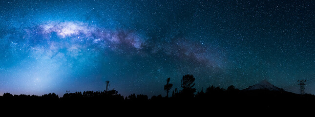 wide panorama of the night sky showing the milky way and the galactic centre. in the foreground are 