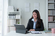 © crizzystudio - Happy young professional employee sitting at work desk with laptop and paperwork in the interior office of modern company using online computer technology startup business idea.