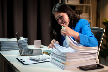 Stressed and tired Asian businesswoman feels a headache while working overtime at night with a pile of documents. Searching, sifting through documents, can't find them. Problems around the office.