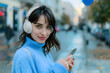 © Андрей Знаменский - Smiling woman in blue sweater uses phone while wearing headphones
