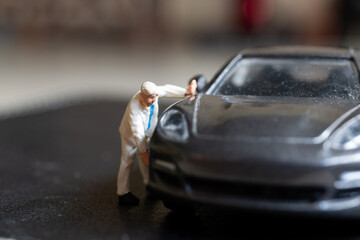 Wall Mural - Miniature people, A worker bends over as if inspecting or repairing something on a sleek metallic gray car model blurred background keeps the focus on the miniature scene